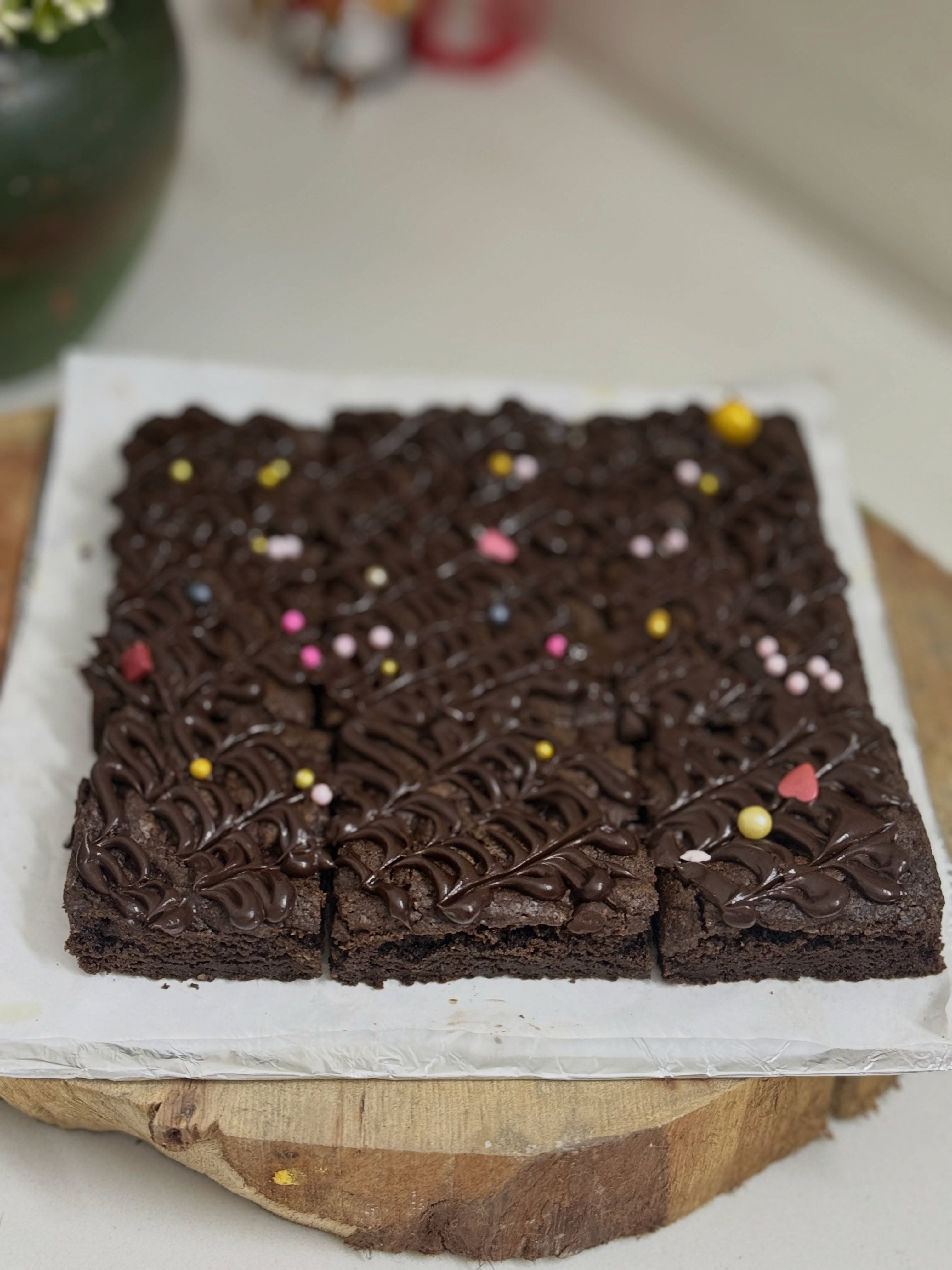 A square cake with dark piped swirls, a pale border, and small colorful decorations.