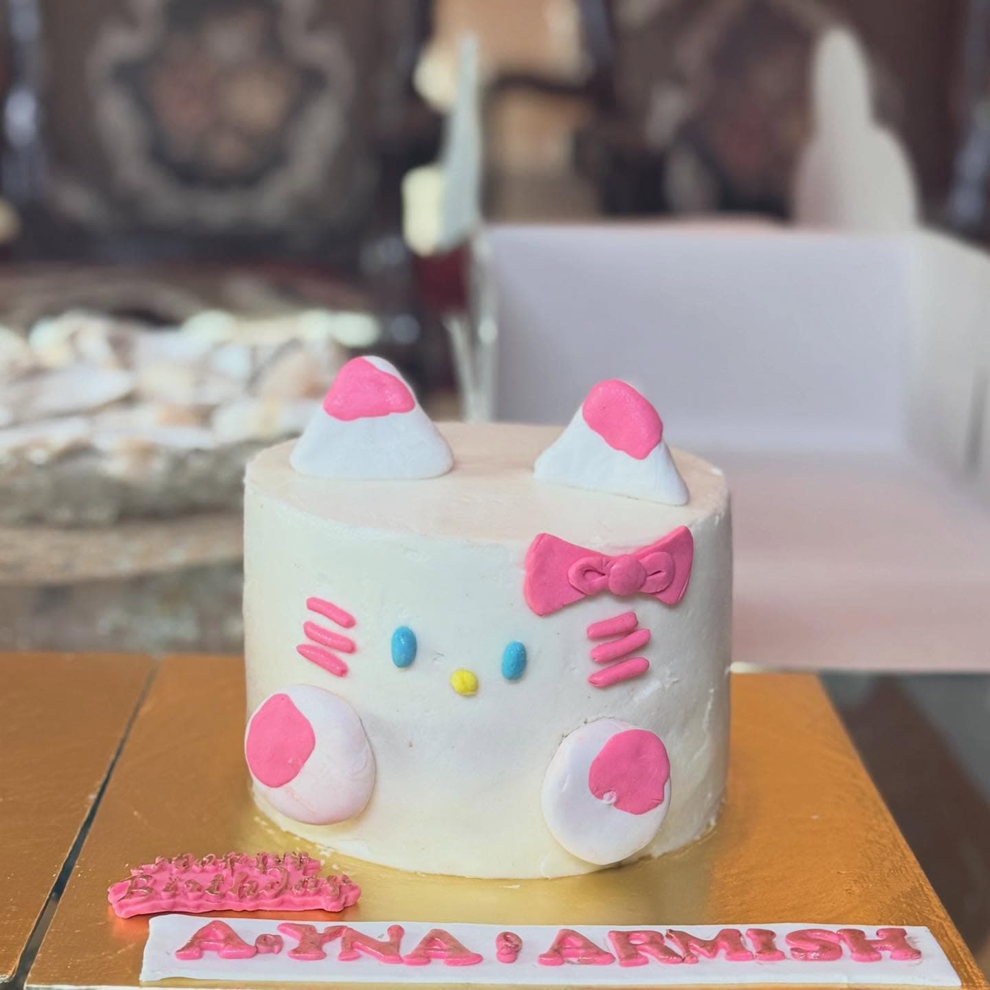 A white cat-face cake with pink ears, whiskers, and a bow.