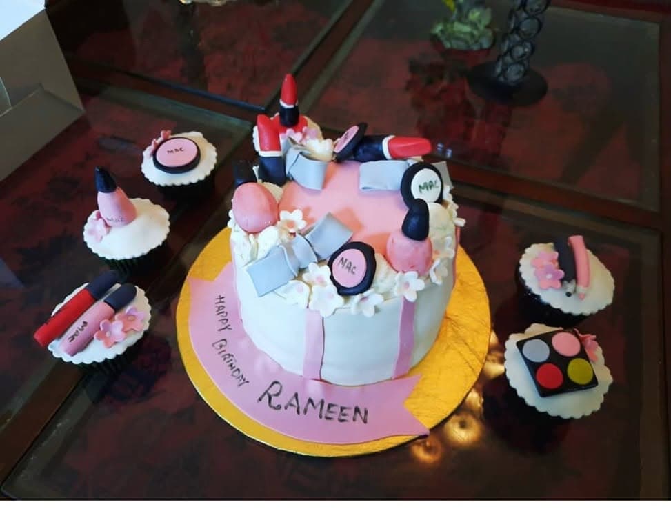 A pale cake decorated with miniature makeup-themed shapes and matching cupcakes.