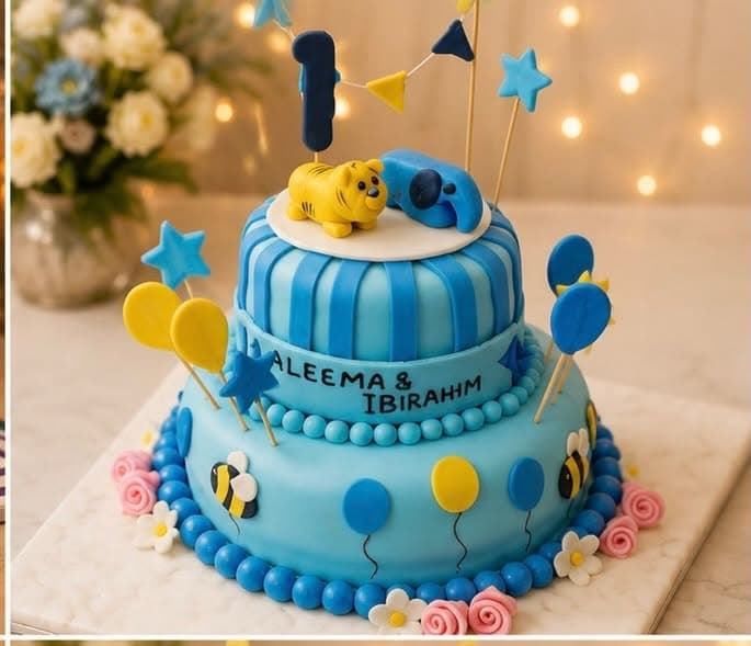 A blue two-tier cake with stars, balloon shapes, small character decorations, and number-one toppers.