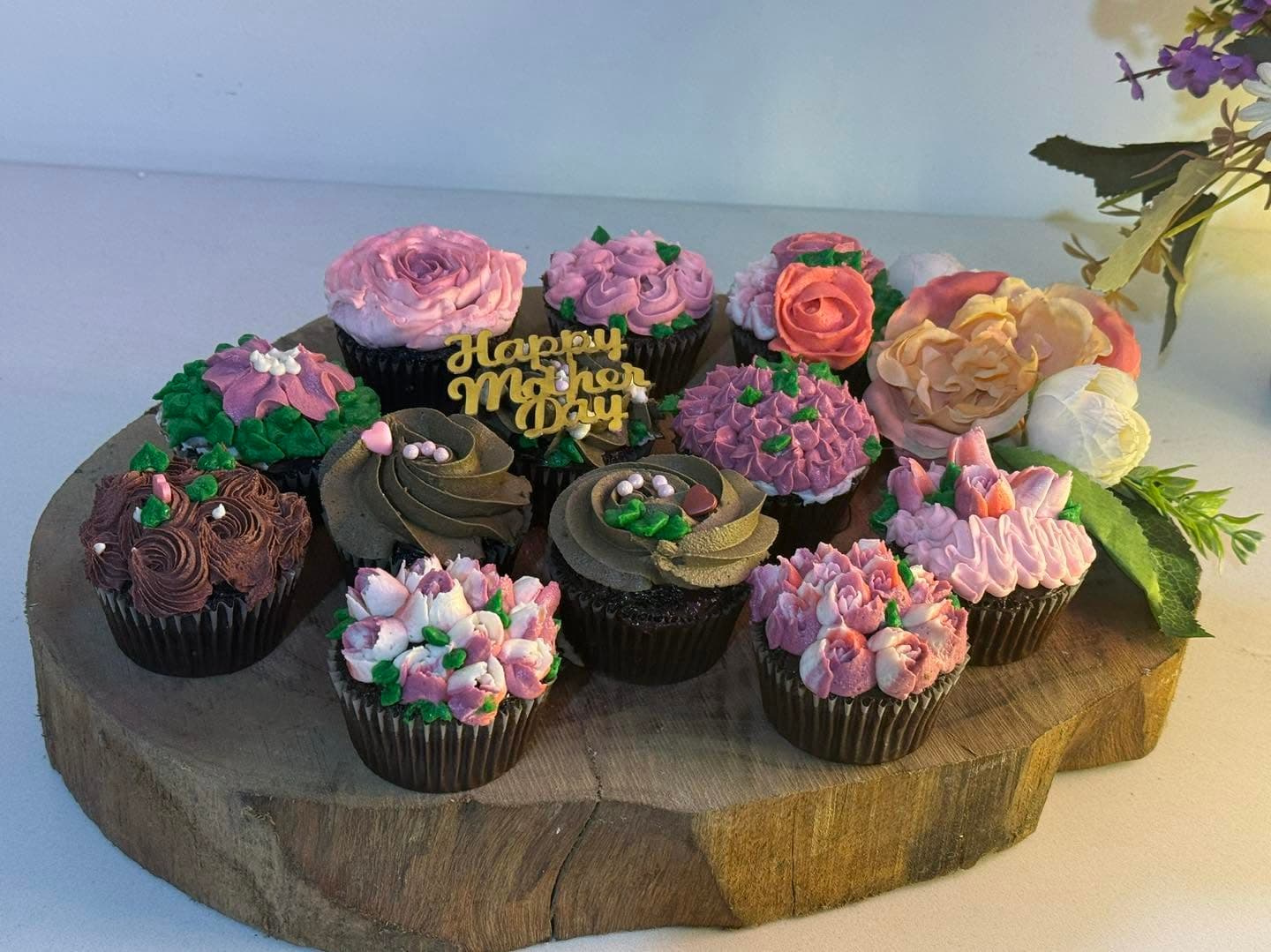 An arrangement of cupcakes with colorful piped flowers on a round wooden board.