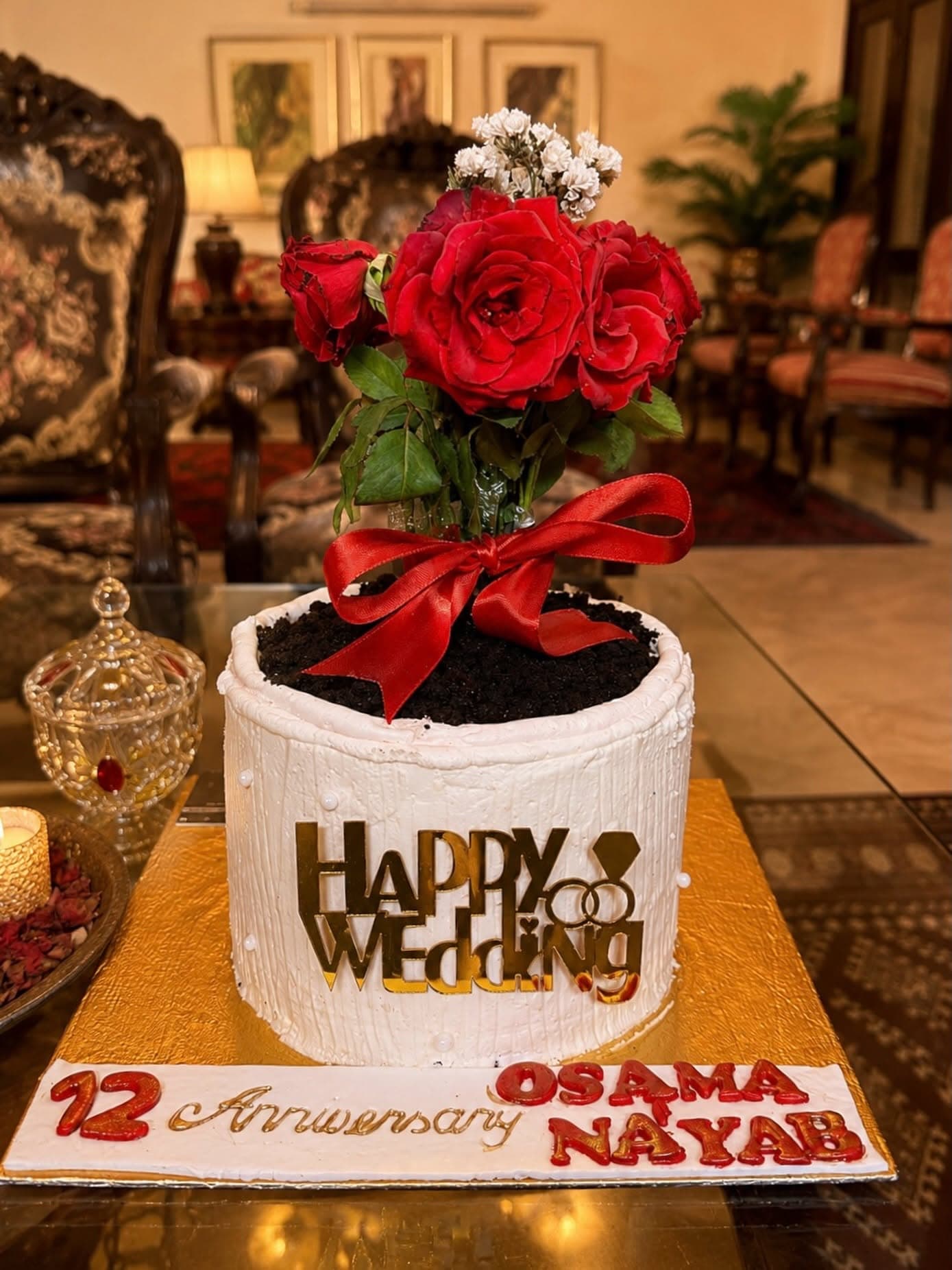 A white cake with red roses, a red ribbon, and gold anniversary lettering.